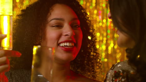 close up of two women in nightclub or bar celebrating drinking alcohol with sparkling lights 2