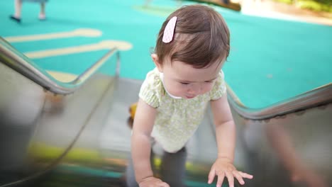 15-month-old mixed race baby girl playing on playground slide. high angle, slow motion