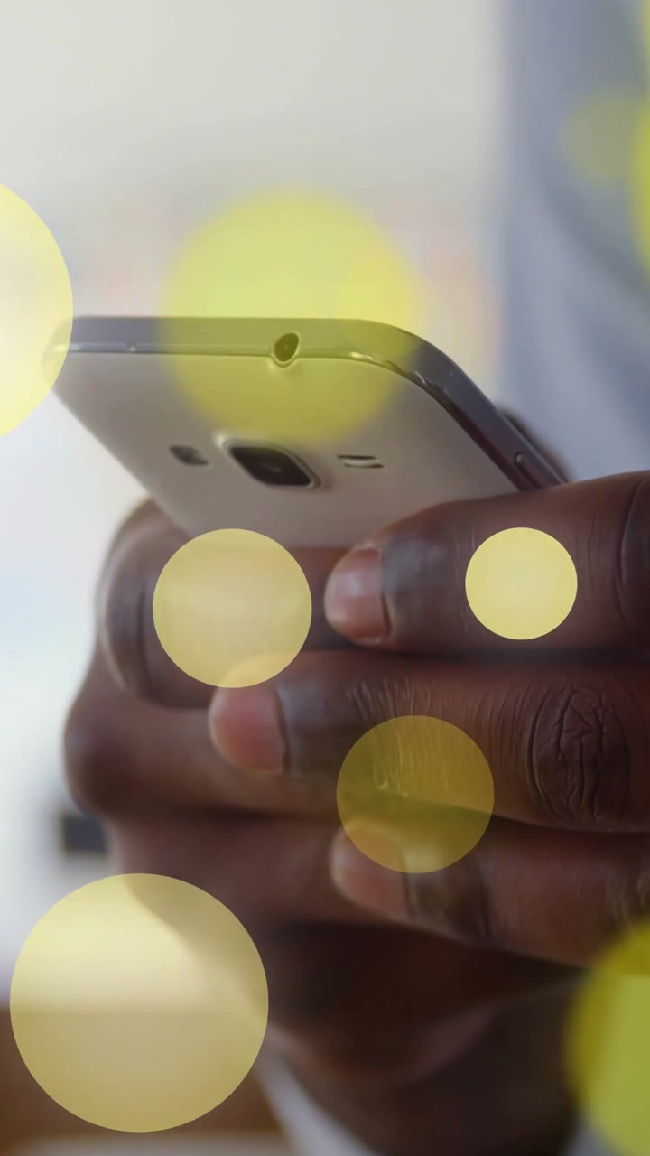 Video verticale: Uomo che tocca lo schermo del telefono, facendo crescere e fluttuare cerchi gialli per una demo tecnologica.