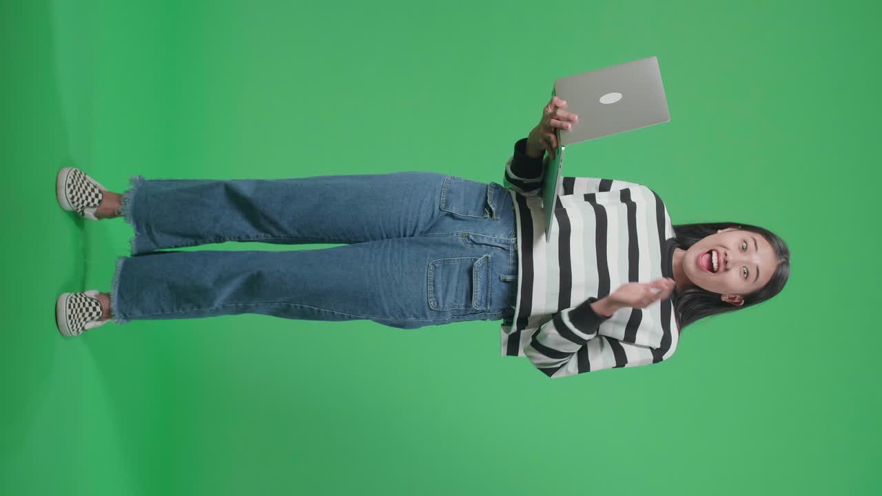 cuerpo lleno de una mujer asiática sonriente sorprendido mientras usa la computadora en el fondo de la pantalla verde