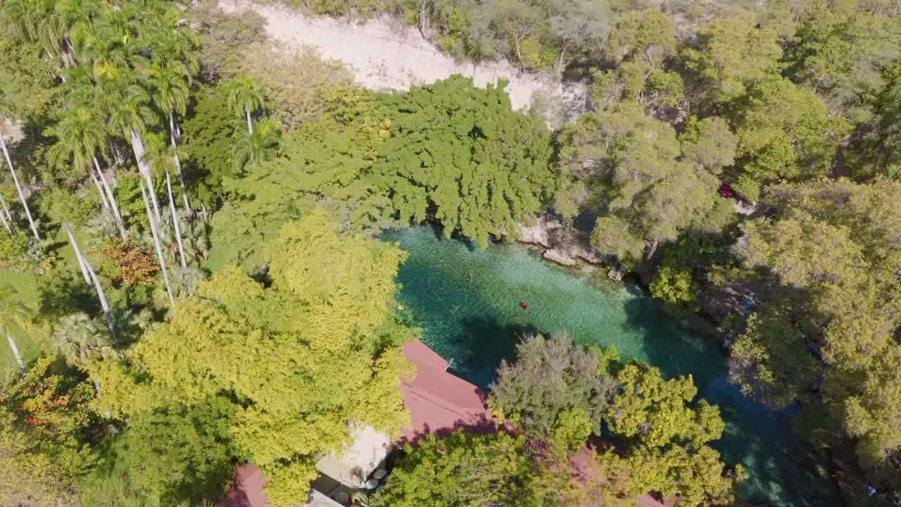 Aerial birds-eye view of people swimming in the turquoise water of Las Marias natural pool, a hidden oasis surrounded by lush jungle, Dominican Republic