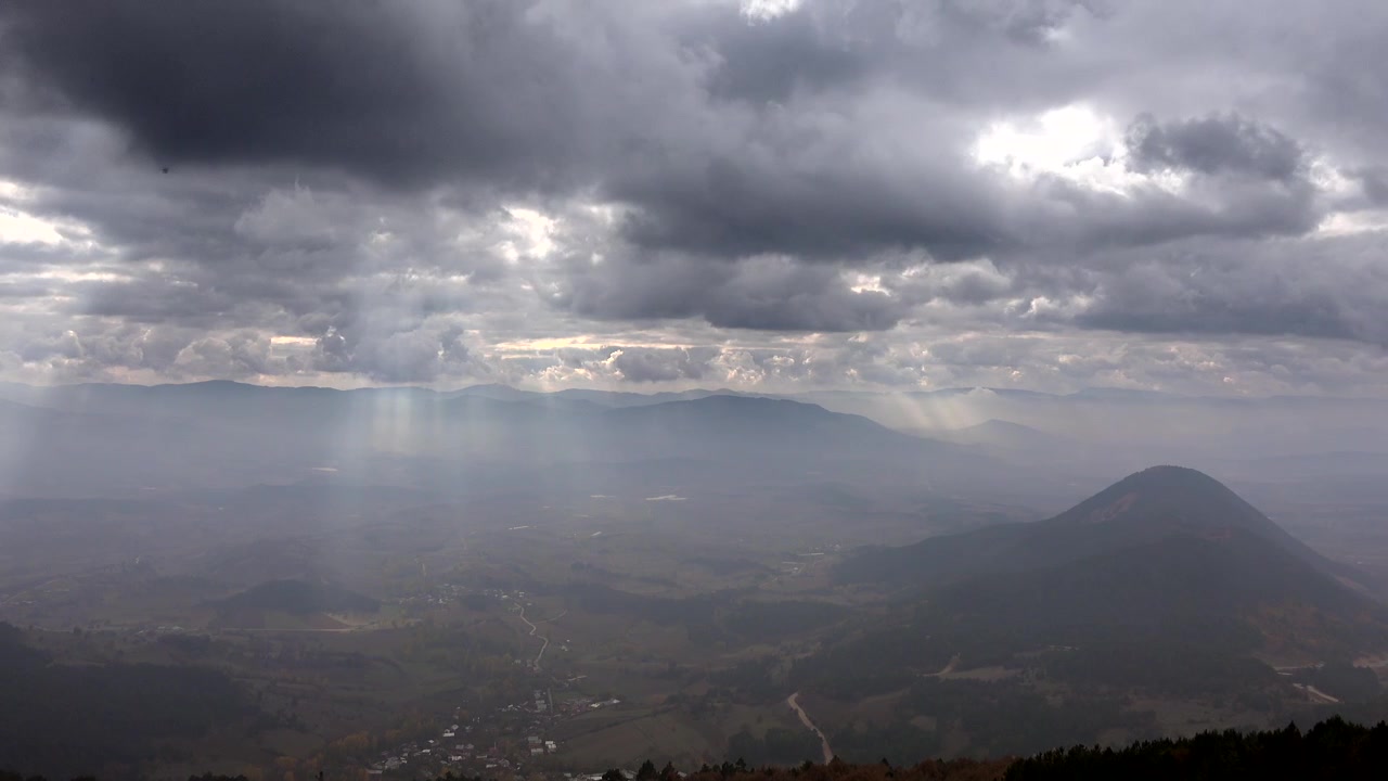 Raggi di sole che filtrano attraverso nuvole temporalesche scure su una valle di montagna