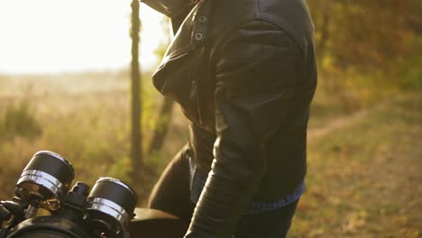 Back-view-of-a-man-in-helmet-and-leather-jacket-coming-up-to-his-bike-and-starting-the-engine-while-standing-on-the-roadside-in