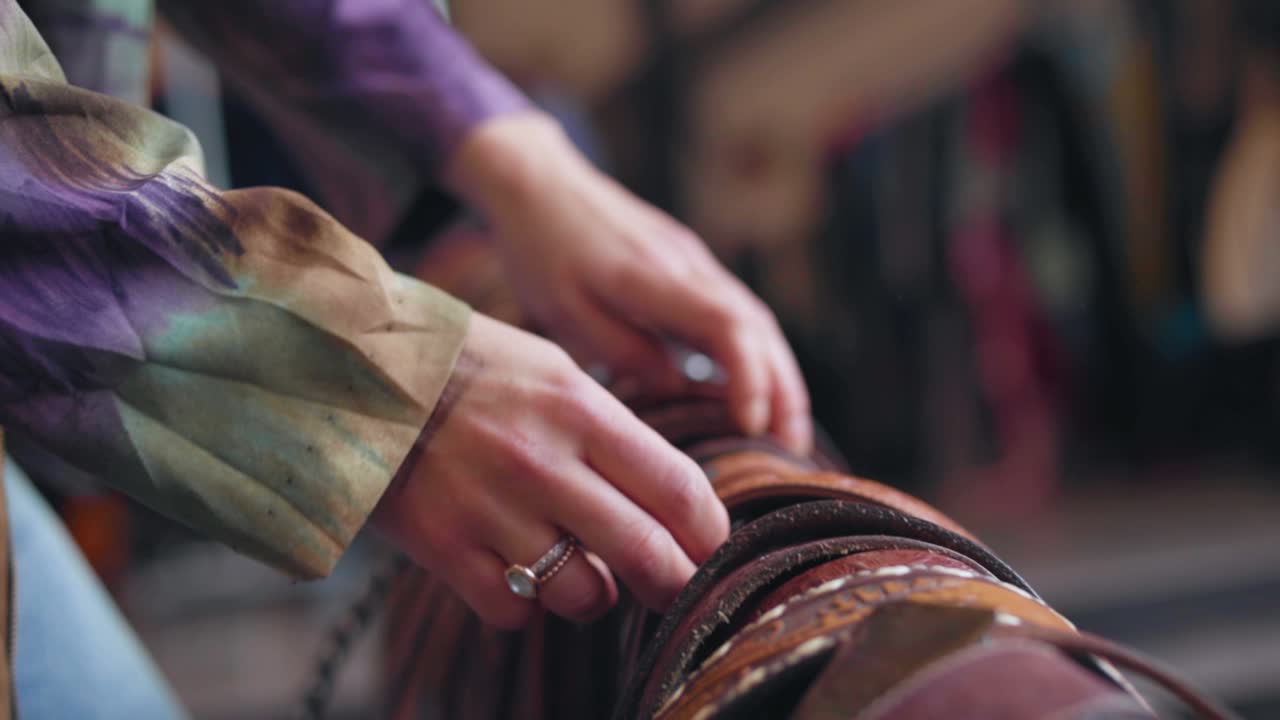 un cliente está comprando en una tienda de ropa de moda de segunda mano en busca de un cinturón de cuero y recorre todo el estante con cinturones que están a la venta con las manos 50 fps