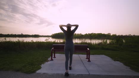 a young, athletic woman wearing a mask places her hands on her head to catch her breath from running