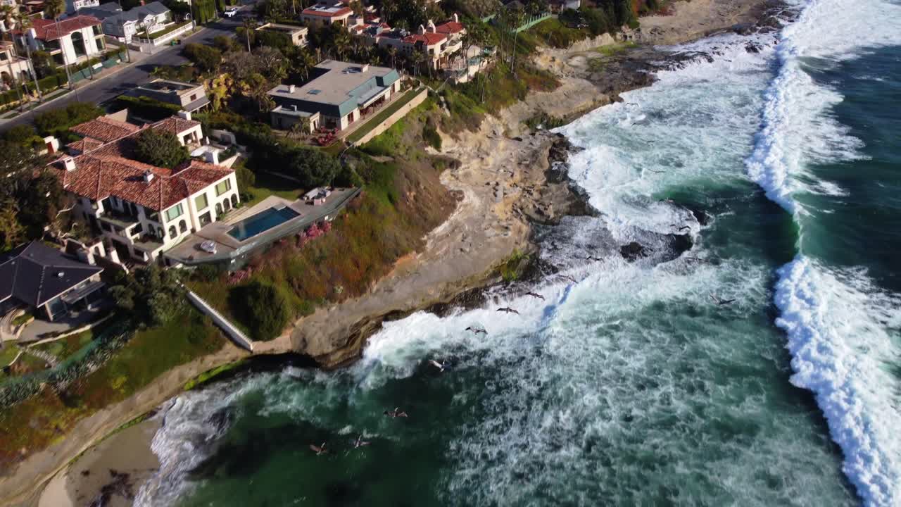 Vista de dron de aves volando sobre aguas costeras y mareales junto a una zona residencial de lujo en primera línea de playa. Playa de La Jolla, San Diego