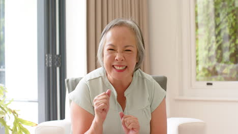 asian senior woman with grey hair smiles with closed eyes, sitting indoors