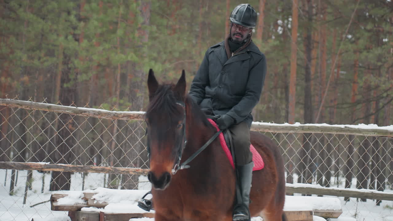 Занятие по обучению верховой езде: инструктор проводит упражнения на заснеженном манеже, тренер демонстрирует специальные техники с послушной лошадью в огороженном заснеженном загоне
