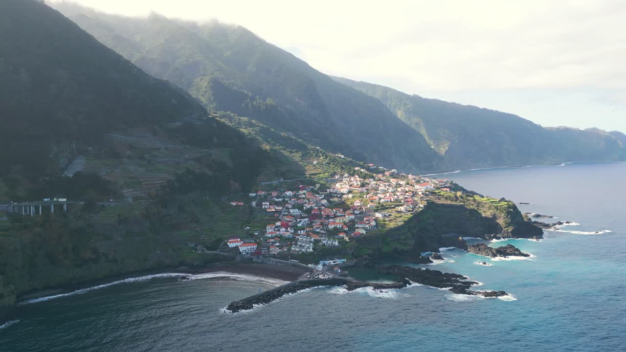 Drone footage flying over the sea towards Seixal, with the sun shining through the mountains, creating a breathtaking scene