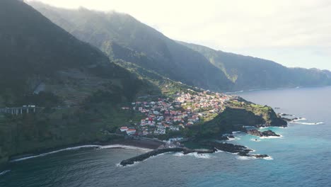 Drone-footage-flying-over-the-sea-towards-Seixal,-with-the-sun-shining-through-the-mountains,-creating-a-breathtaking-scene