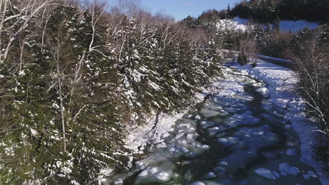 rising-drone-shot-of-icy-and-flowing-winter-river-to-reveal-mountains