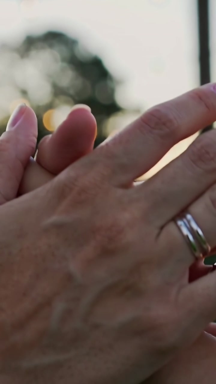Vertical video: Cam panning two hands locking fingers in park at dusk showing love with jewelry