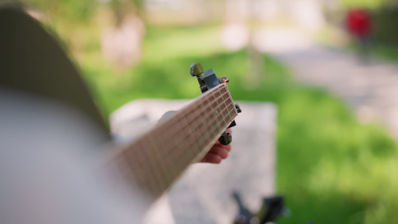 Tuning guitar on park bench. Quietly adjusting acoustic guitar in park. Person finetuning guitar on bench in park. Casual morning moment of tuning and practicing acoustic guitar outdoors