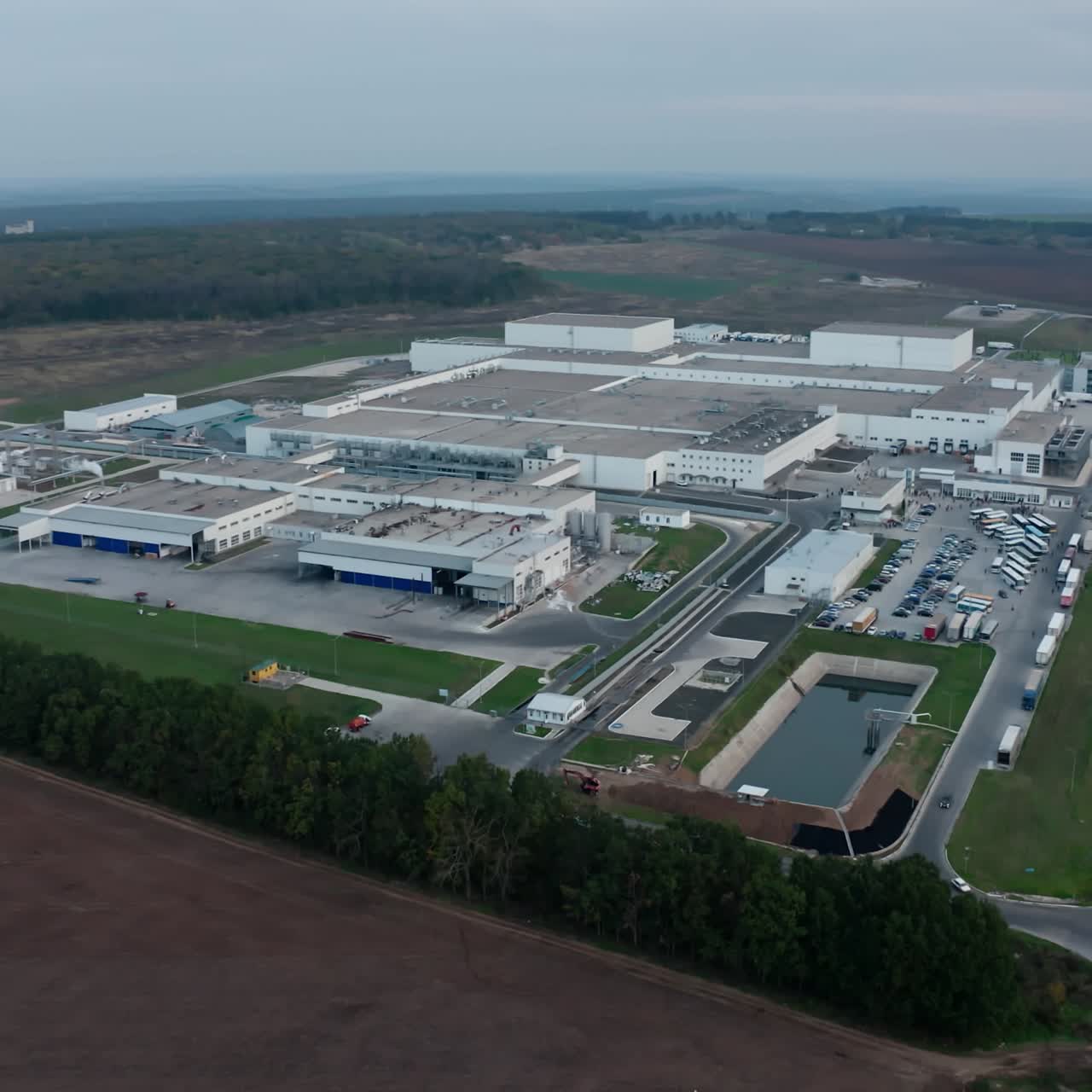 Modern industrial zone outdoors. Large factory with many buildings and cars moving on the road. Manufacturing on beautiful nature background. Aerial view.