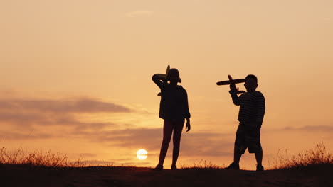 silhouettes of a girl and a boy playing together with airplanes at sunset a happy and carefree child