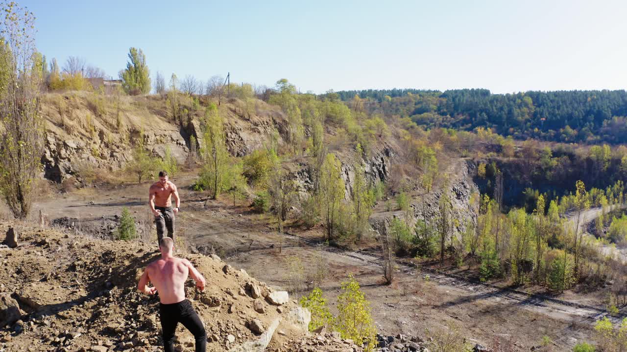 Muscular sportsmen are exercising on nature background. Athletic shirtless men training outdoors. Sporty guys showing their strength body. Aerial view.