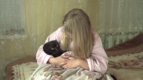 school-age girl rocks cat wrapped in blanket in her arms.