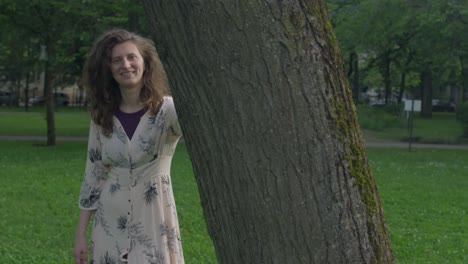 young beautiful woman standing next to a tree smiling to the camera