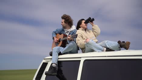 un niño toca la guitarra y una niña mira a su alrededor con unos binoculares en el techo de una caravana.