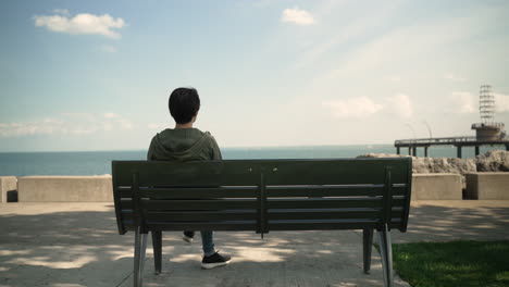 woman with short hair sits on a bench overlooking a lake and a pier