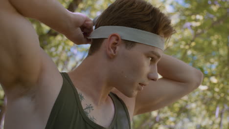 young man wears headband while looking towards a direction, staying vigilant and focused, ready to face whatever challenges lie ahead in an outdoor environment surrounded by trees