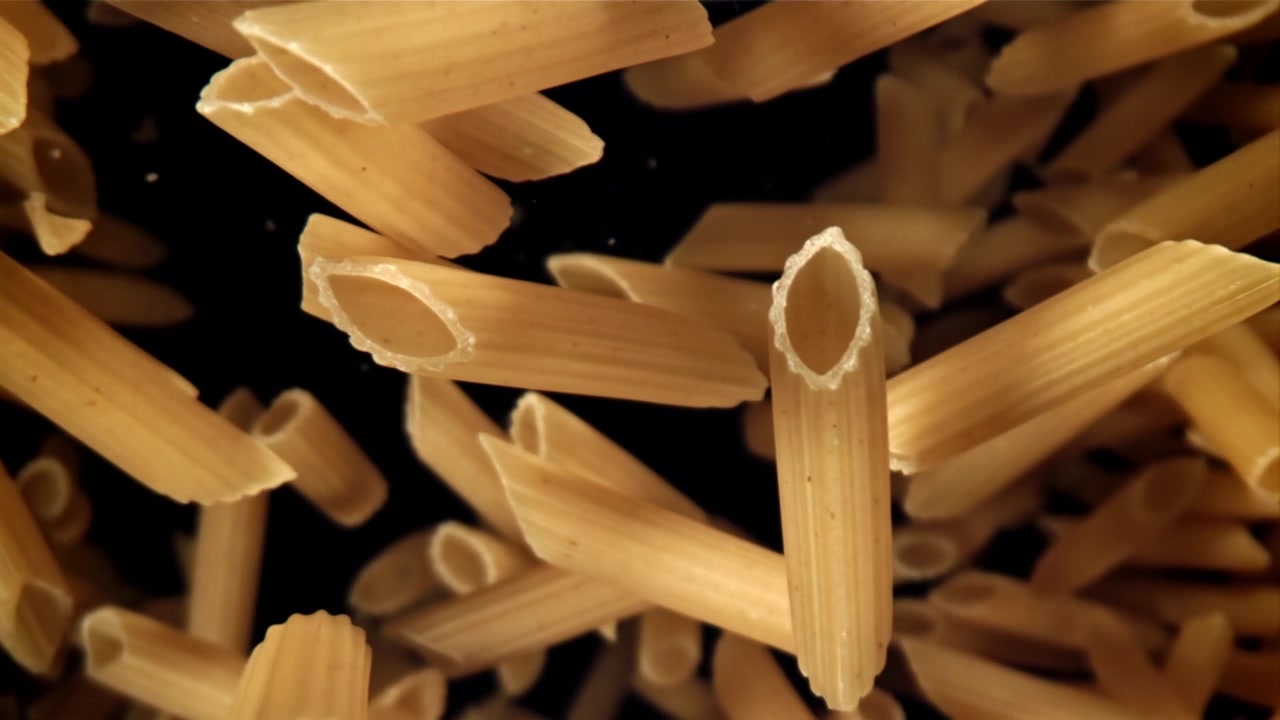 Penne secche che cadono al rallentatore su sfondo nero
