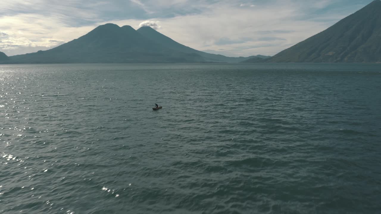 Droneoptagelse fra luften af Atitlan-søen, vulkaner og en lokal mand der ror kajak i Guatemala
