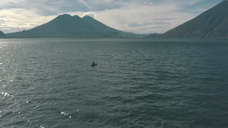 drone aerial shot of lake atitlan, volcanoes and a local man kayaking in guatemala