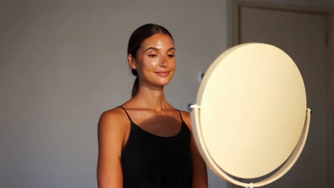 A woman looks at her reflection in a mirror, showcasing her glowing skin