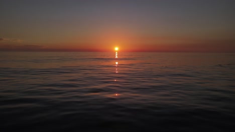 drone shot flying over calm ocean with golden sun setting in the middle