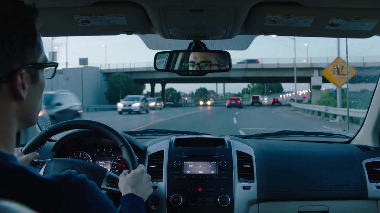 Driving driver with glasses and sweater checking mirror while left car passing near overpass