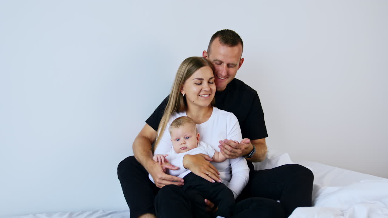 Giovane coppia caucasica seduta con il loro bambino in braccio. Il papà tiene la manina del bambino. Sfondo bianco.