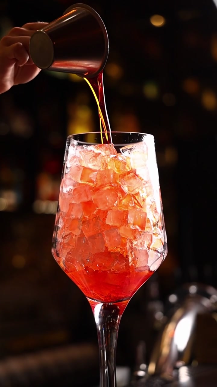 Barista che versa un cocktail rosso in un bicchiere pieno di ghiaccio