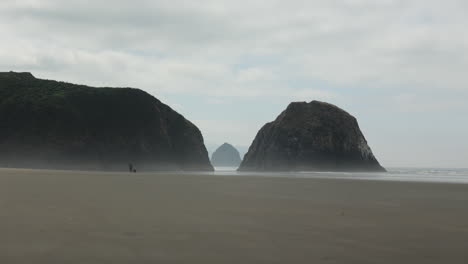 Día-Tranquilo-En-La-Playa-Crescent-En-El-Parque-Estatal-Ecola-Con-Una-Persona-Y-Un-Perro-Caminando-En-La-Playa