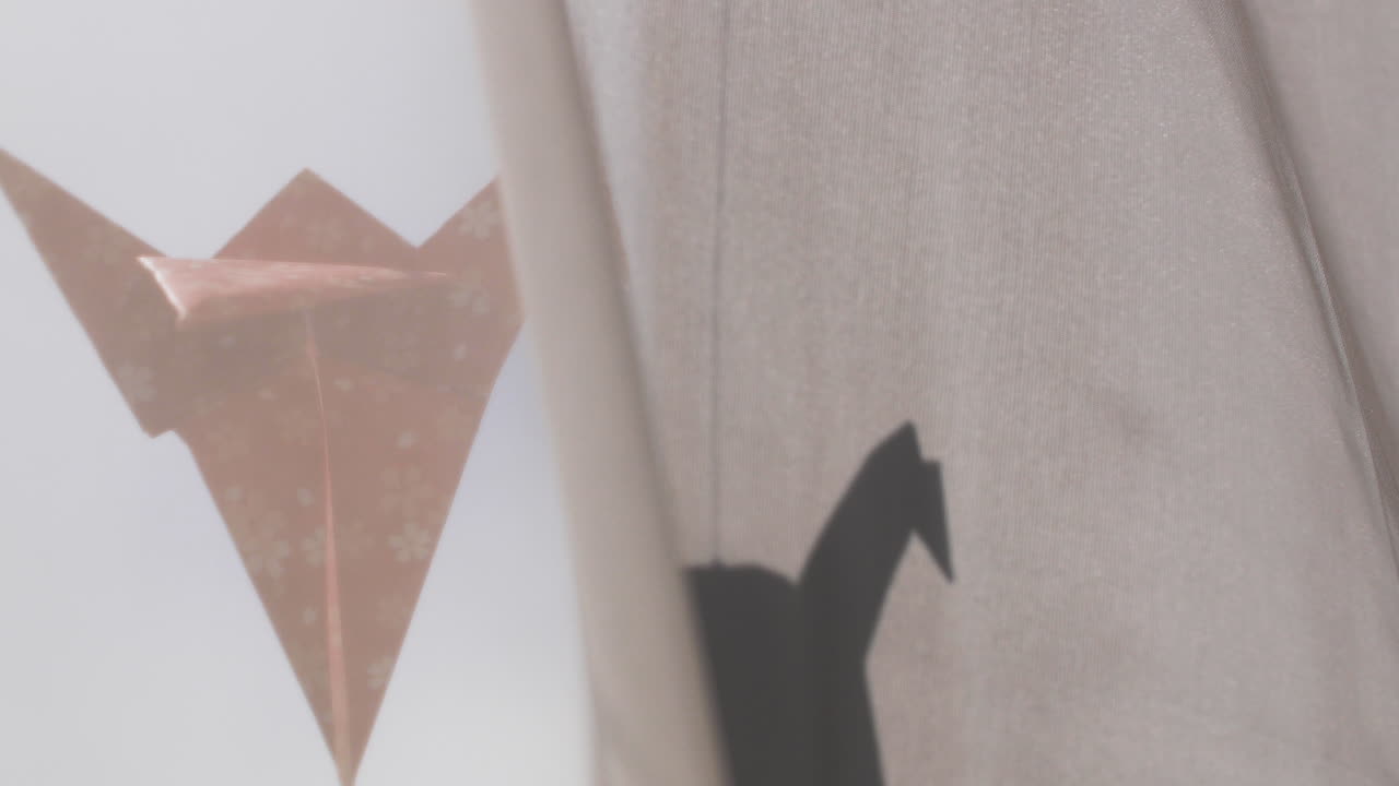 Red origami crane hangs in the window. Its silhouette is casted onto the curtain