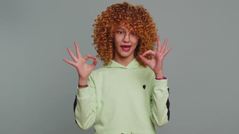 Young teen school girl in glasses looking approvingly at camera showing okey gesture like sign
