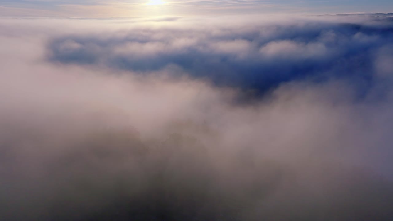 Drone flies over soft, pale clouds as dawn brightens the horizon.
