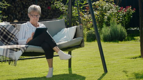 portrait of senior woman using a tablet. sitting in a garden swing in the backyard of a house