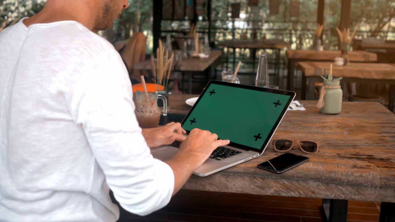 closeup de manos masculinas trabajando en una computadora portátil con pantalla verde en una cafetería