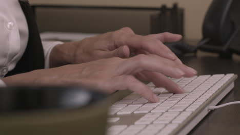Caucasian female executive types at her computer in an office setting with out of focus coffee mug in the foreground