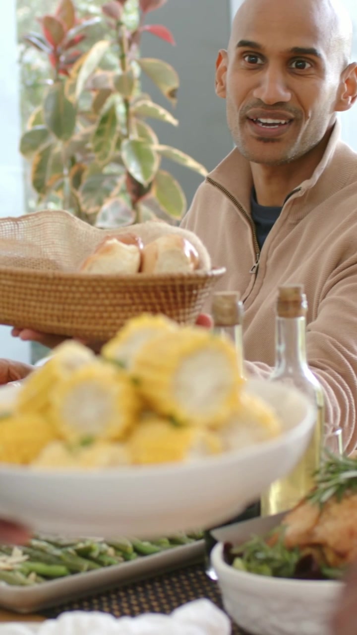Video verticale: Uomo che passa un cestino a tavola in famiglia mentre una donna in verde serve il mais, spazio per il testo.