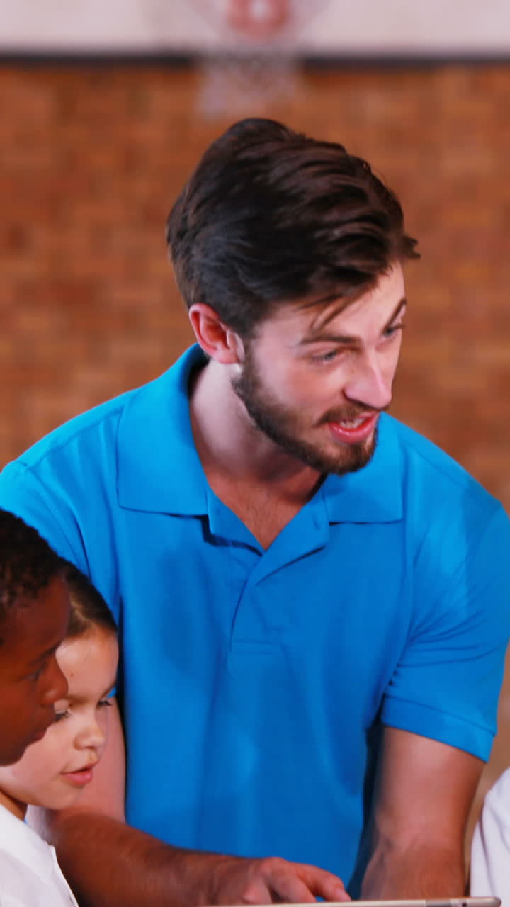 maestro de deportes enseñando a los niños en una tableta digital en la cancha de baloncesto