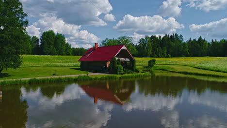 Cabaña-De-Madera-Con-Techo-Rojo-A-Orillas-Del-Lago-En-Un-Paisaje-Verde-Bucólico-E-Idílico