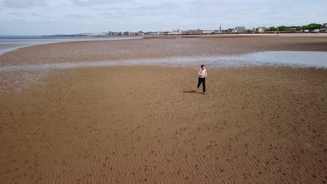 Young-shirtless-adult-male-running-on-a-beach-next-to-the-sea,-aerial