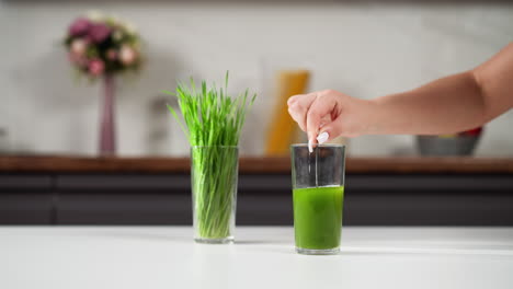 mano colocando una paja en un vaso de jugo verde, hierba de trigo en el fondo