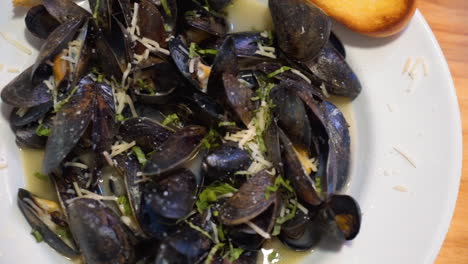 Plate-of-freshly-steamed-mussels-in-white-wine-sauce-with-herbs-and-cheese,-close-up-slider-HD