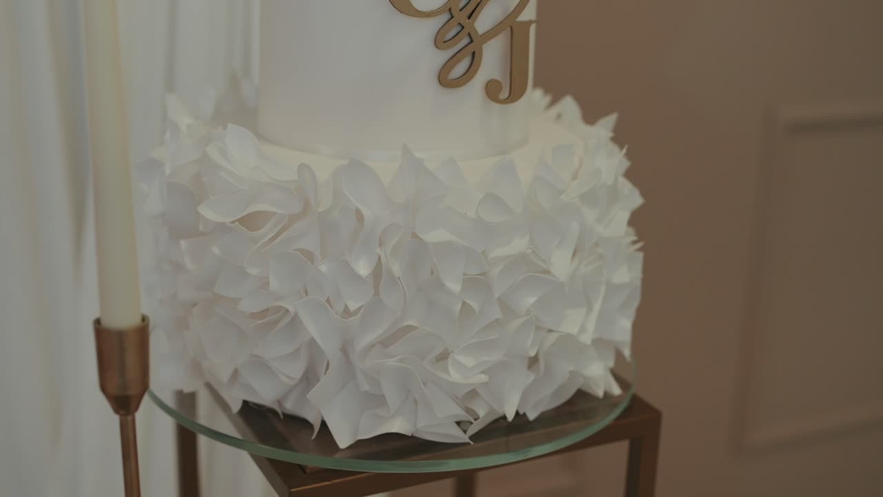 close up of white wedding cake with layered sugar petals and golden monogram topper