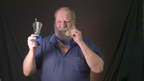 old bearded man winning a gold medal and showing off his trophy