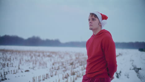 Nachdenklicher-Mann-In-Roter-Kapuzenjacke-Und-Weihnachtsmütze-Steht-Auf-Einer-Schneebedeckten-Landschaft