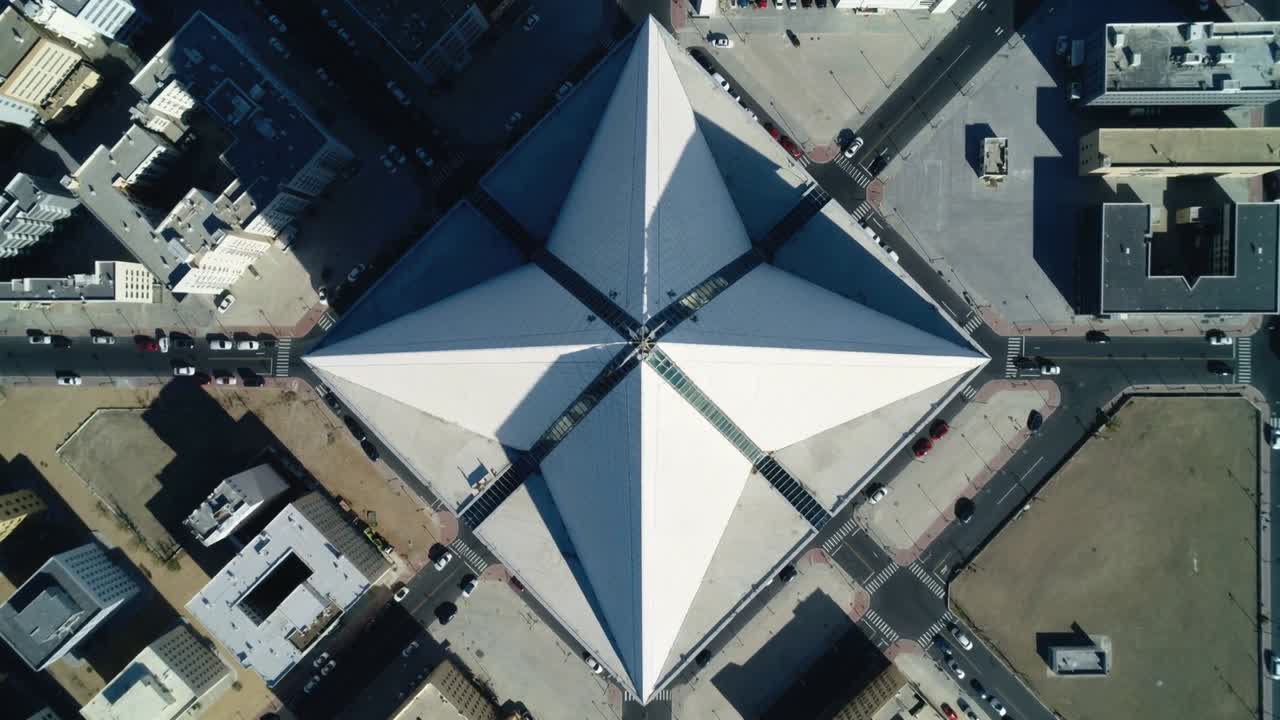 Drone in hovering che cattura un tetto bianco a quattro punte sopra un isolato urbano, mostrando ombre in movimento e auto